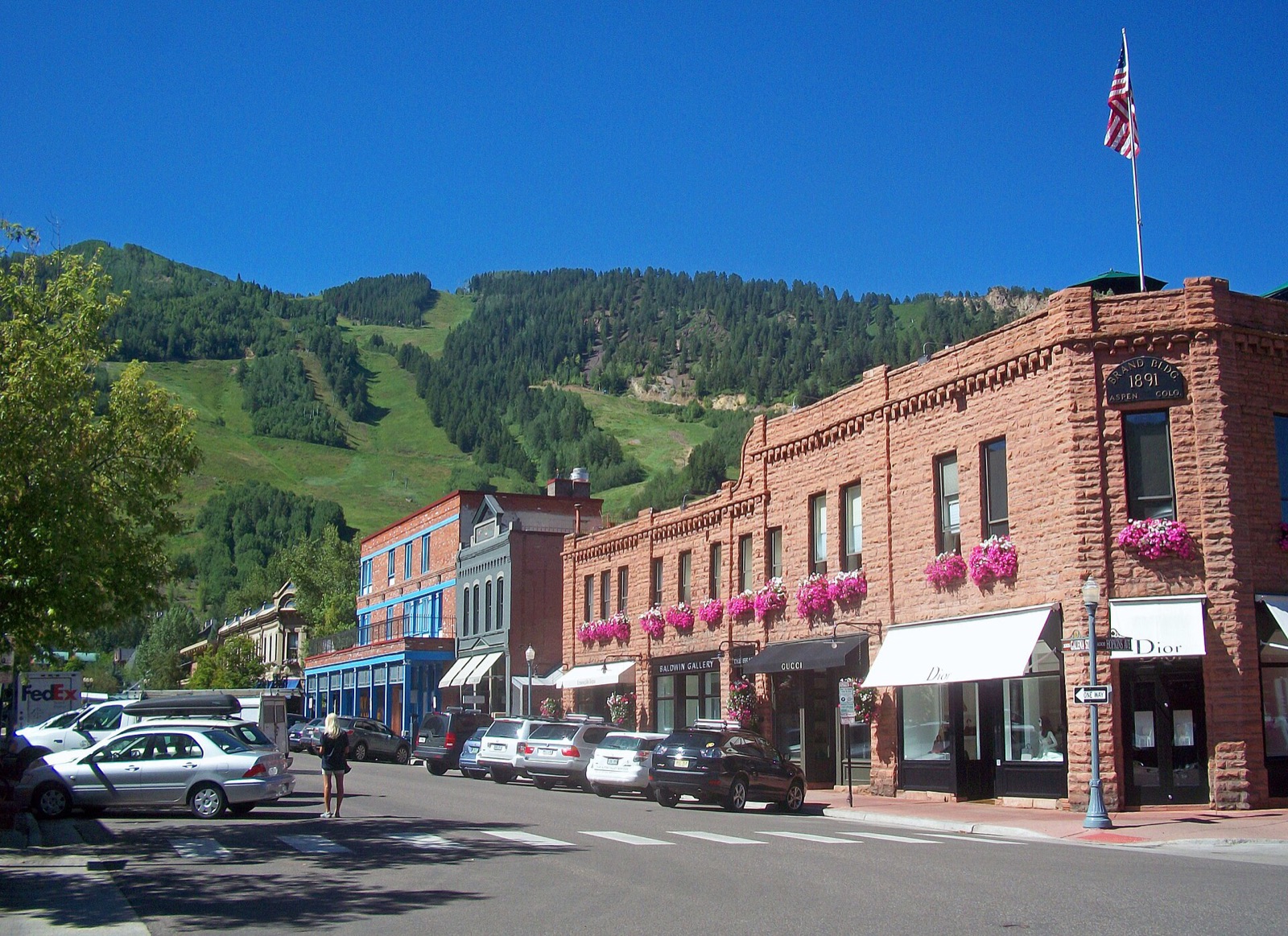 Brick Victorian storefronts on a downtown Aspen street with Aspen Mountain rising green behind the rooftops
