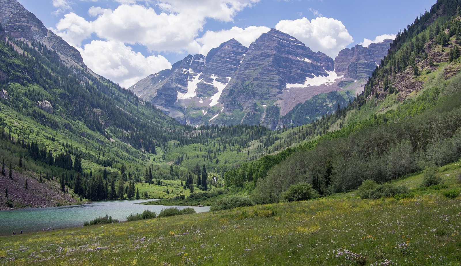 The Maroon Bells peaks above Maroon Lake in summer, with green meadows and conifer forest in the valley below